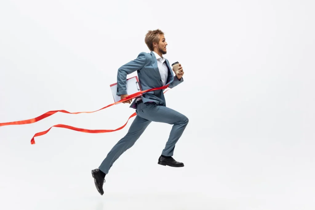 An energetic businessman in a suit leaps past a finish line ribbon while holding a coffee, symbolizing a successful start in a new role, as recommended by JOH Partners.
