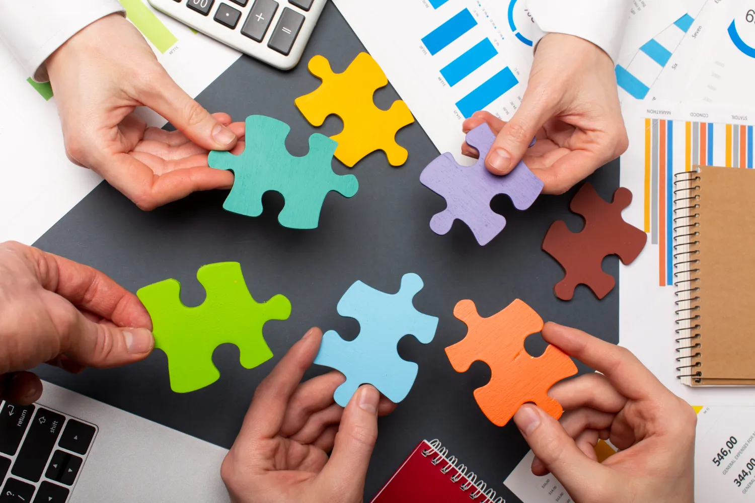 Hands of a diverse team fitting colorful puzzle pieces together, symbolizing JOH Partners' strategy for fostering a dynamic workplace culture.