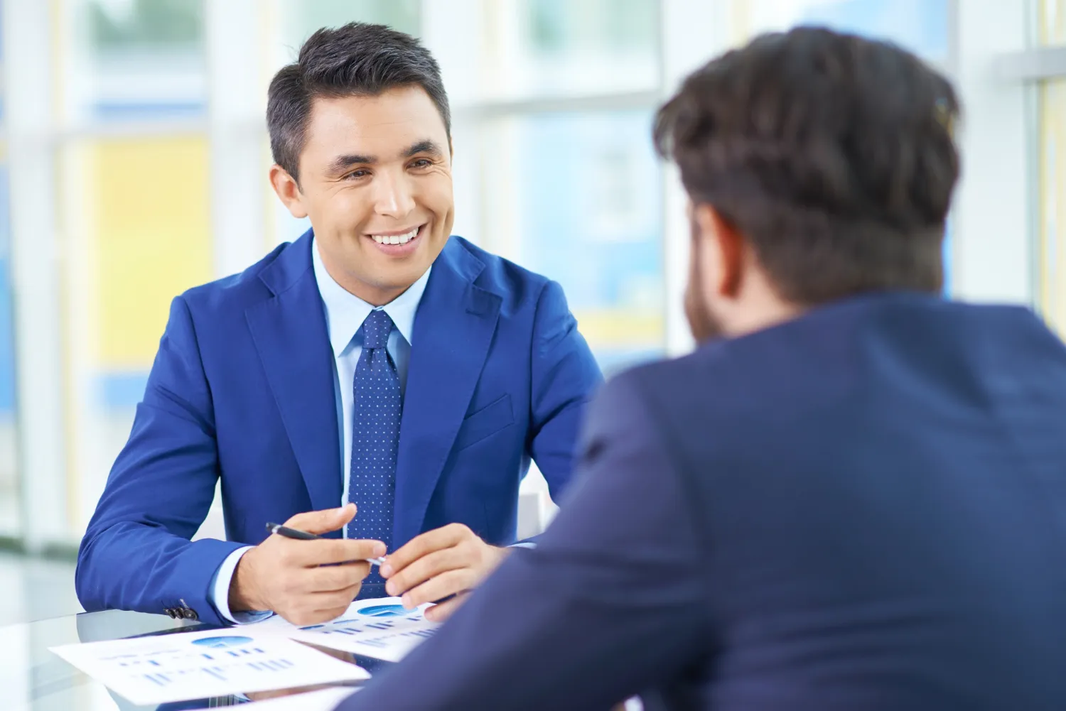 A smiling professional in a blue suit conversing with a colleague, representing the positive impact of effective feedback techniques offered by JOH Partners.