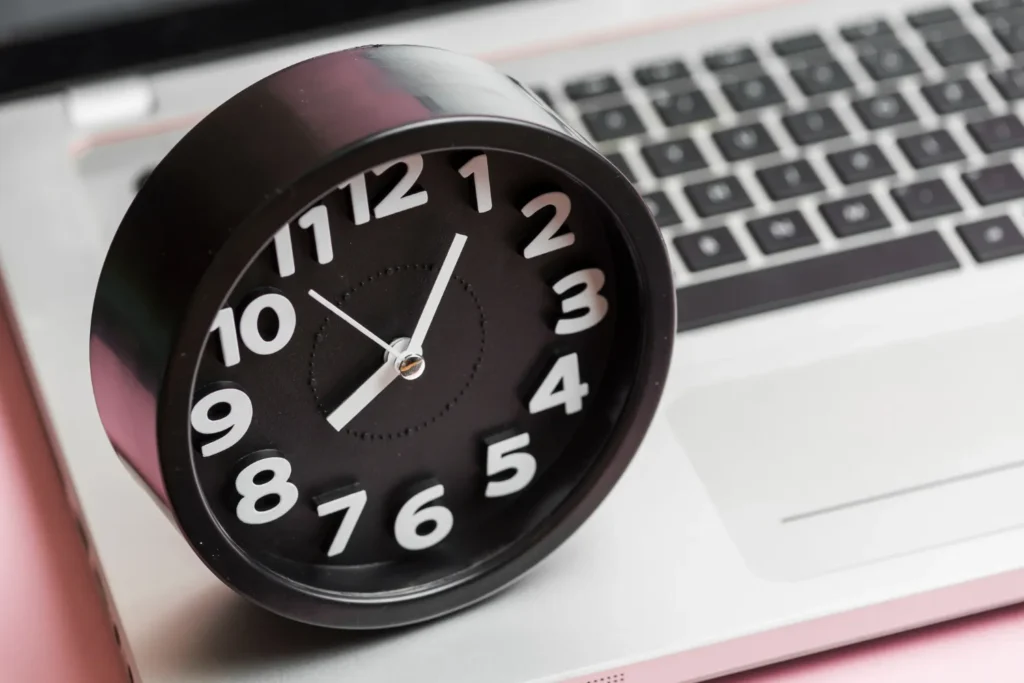 A black analog clock on a laptop keyboard, symbolizing the importance of time management in professional growth with JOH Partners.
