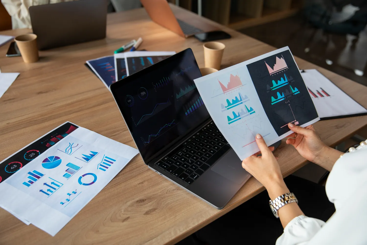 An individual reviews data charts and analytics on printouts and a laptop, representing JOH Partners' focus on big data analytics for strategic insights.